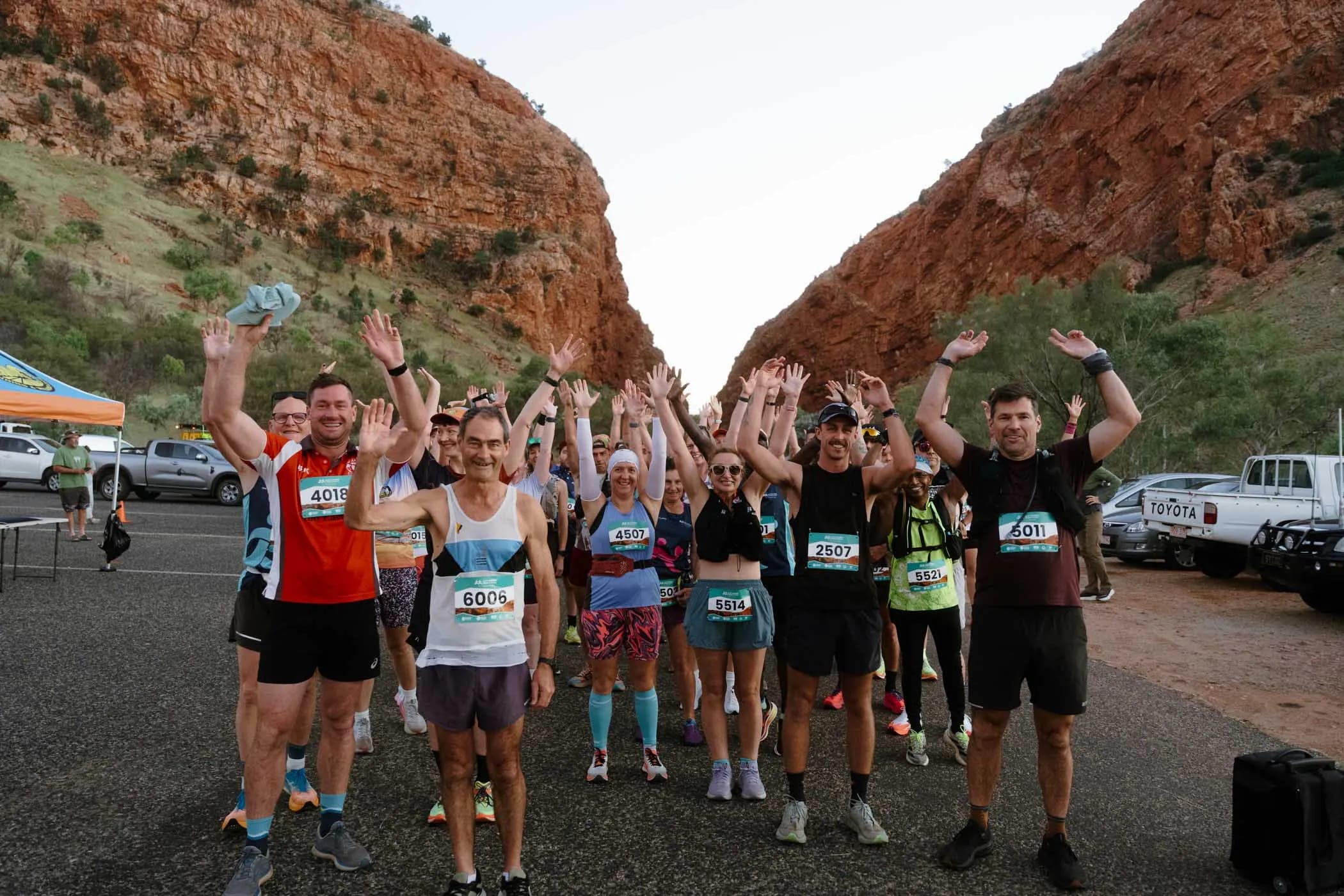 A group of runnings with arms raised at the start of a running race at the Alice Springs Masters Games