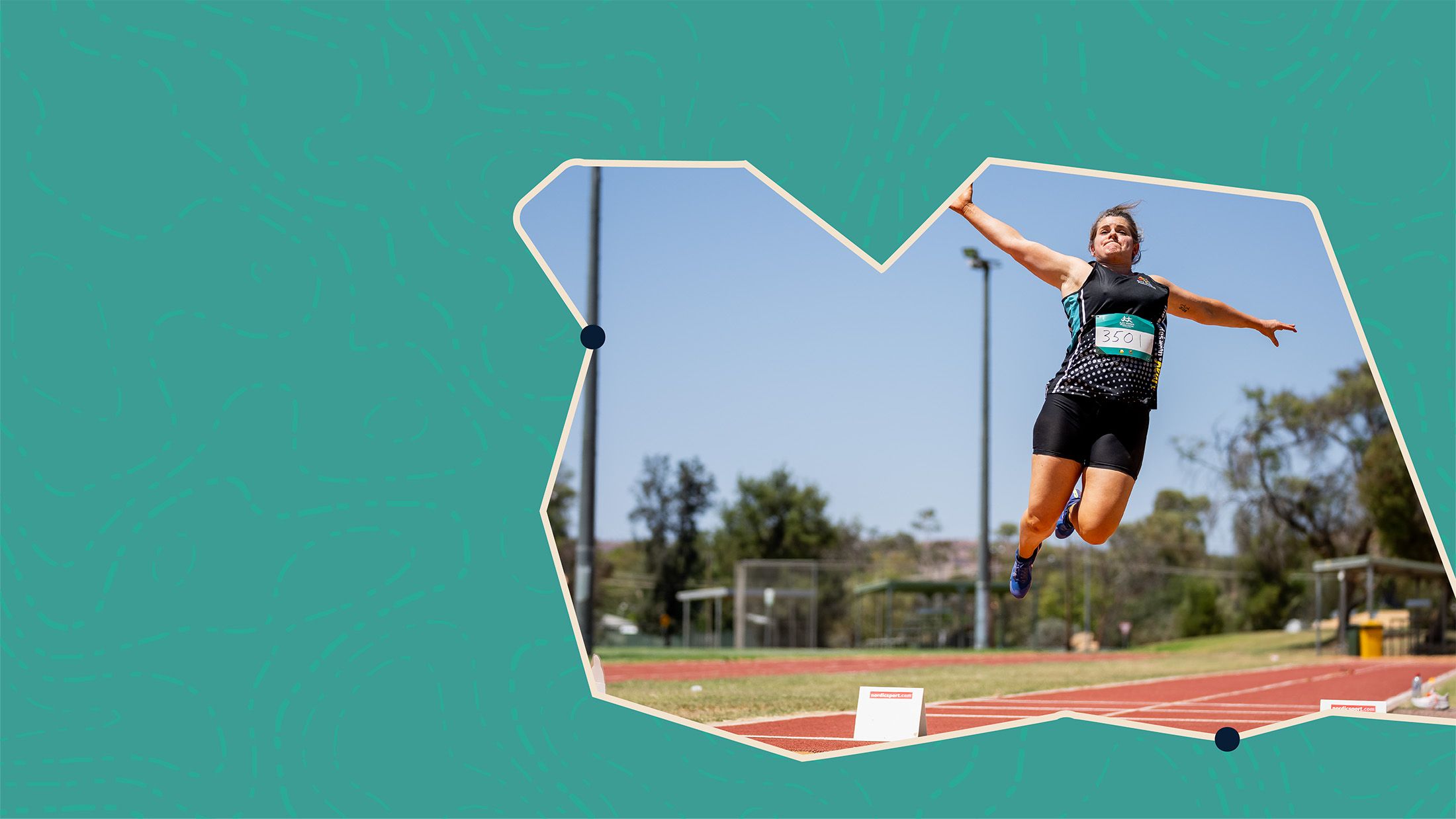 Athlete in mid-air during a long jump on a track field, with a clear blue sky and trees in the background.
